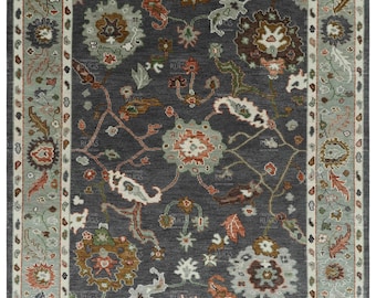 May include: A gray area rug with a floral pattern in shades of brown, green, and white. The rug has a border with a repeating pattern of leaves and flowers.