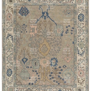May include: A rectangular rug with a central beige field, adorned with detailed floral and geometric patterns in blue, pink, and beige. The rug features a patterned border with repeating motifs and the text "CRAFTSMAN RUGS DECOR THE HOME".