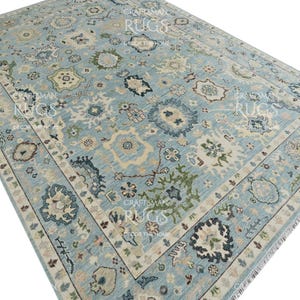 Pu&ograve; includere: Un grande tappeto rettangolare con sfondo azzurro e un intricato motivo floreale nei toni del crema, verde e blu navy. Il tappeto presenta un bordo dettagliato e frange lungo i bordi, aggiungendo consistenza e interesse visivo. Misura circa 240 x 300 cm.