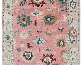 May include: A pink rug with a floral pattern in shades of teal, brown, and cream. The rug has a border with a geometric design.