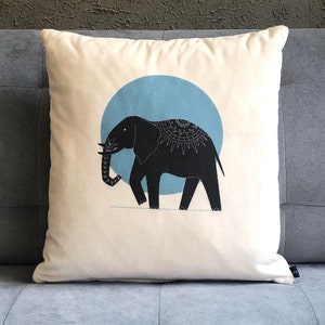 May include: A white cushion with a black elephant silhouette on a blue circle. The elephant has a decorative pattern on its back.