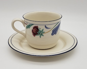 May include: A white teacup and saucer with a blue rim and floral design. The cup has a floral pattern with red, blue, and green accents.