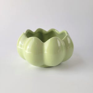 May include: A light green ceramic planter with a scalloped rim. The planter has a rounded, pumpkin-like shape and a glossy finish. This decorative piece is suitable for small plants or succulents.