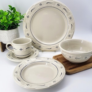 May include: A set of cream-colored ceramic dinnerware with a blue and white floral pattern. The set includes a dinner plate, a salad plate, a bowl, and a teacup and saucer.