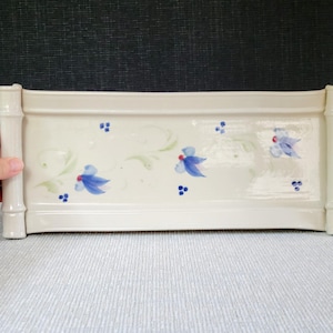 May include: Cream-colored rectangular ceramic planter with bamboo-style corner posts. The planter is decorated with blue floral and green leaf designs. The planter is on a light blue surface.