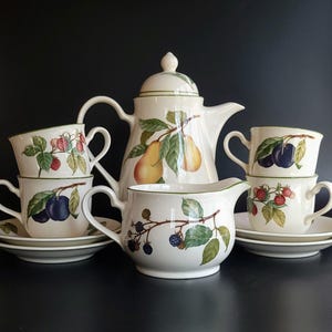 May include: A white ceramic mug with a black handle and the text "But First, Coffee" in a black, handwritten-style font. The mug is on a white surface.