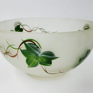 May include: A frosted glass bowl with hand-painted green ivy leaves and brown vines. The bowl has a wide, rounded shape and a small, circular base. The ivy design is repeated around the bowl's exterior.