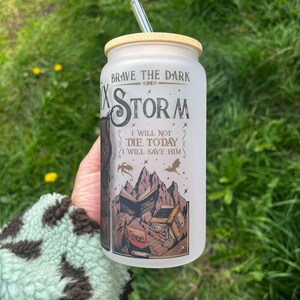 Peut inclure: Un gobelet en verre d&eacute;poli avec un couvercle en bambou et une paille argent&eacute;e. Le gobelet pr&eacute;sente le texte "Brave the Dark" et "Storm" avec un graphique de montagne et de livre. Le design comprend le texte "I will not die today, I will save him."
