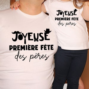 K&ouml;nnte beinhalten: Zwei wei&szlig;e T-Shirts mit schwarzem Text, der "Joyeuse Premiere Fete des Peres" lautet. Der Text ist auf Franz&ouml;sisch und bedeutet "Frohes erstes Vaterfest".