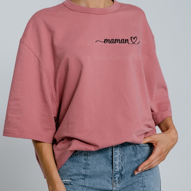 May include: A pink oversized t-shirt with the text "maman" and a heart symbol in black.