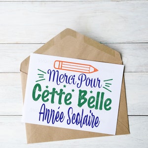 May include: A white card with blue text that says "Merci Pour Cette Belle Ann&eacute;e Scolaire" with a green and orange pencil above the text.