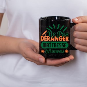 May include: Black coffee mug with a green and orange design that says "Ne Pas Deranger Maitresse En Vacances".