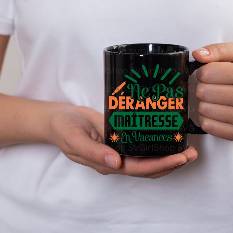 May include: Black coffee mug with a green and orange design that says "Ne Pas Deranger Maitresse En Vacances".