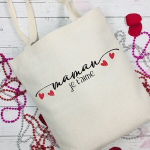 May include: A white canvas tote bag with black text that reads "maman je t'aime" and three red hearts.