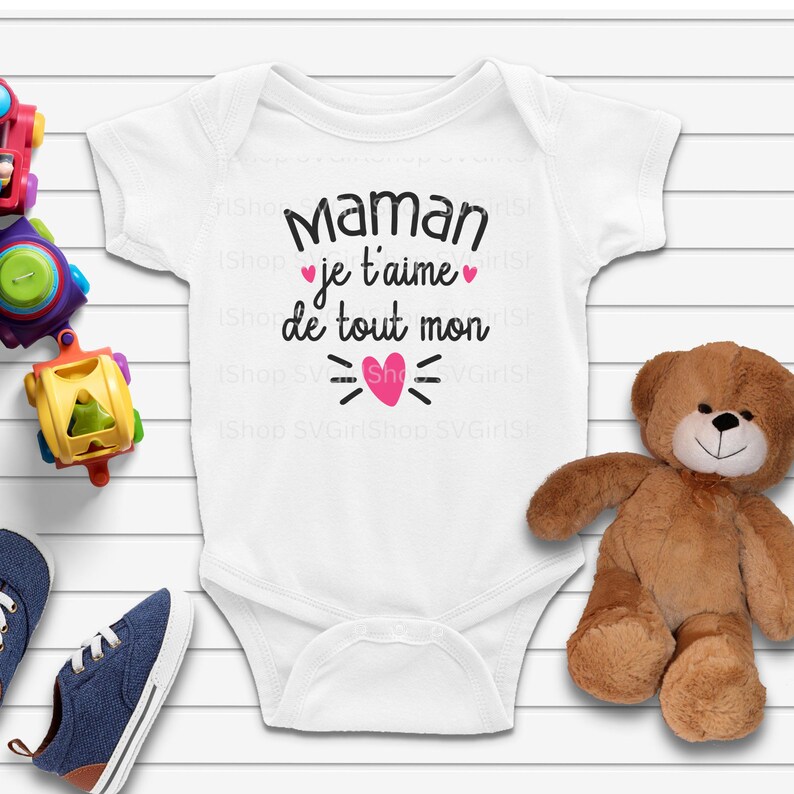 May include: White baby onesie with the text "Maman je t'aime de tout mon" in black with a pink heart graphic.