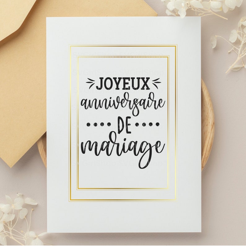 May include: A white card with a gold frame and the text "Joyeux anniversaire de mariage" in black script.