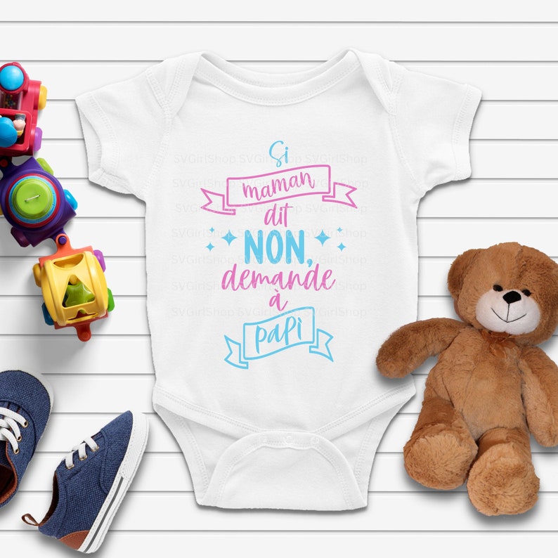 Peut inclure: Body de b&eacute;b&eacute; blanc avec l'inscription "Si maman dit NON, demande &agrave; papi" en rose et bleu. Un ours en peluche, des voitures jouets et des chaussures de b&eacute;b&eacute; bleues entourent le body.