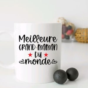 May include: White ceramic mug with a black inscription that reads "Meilleure Grand-Maman du monde" with two red stars and hearts.