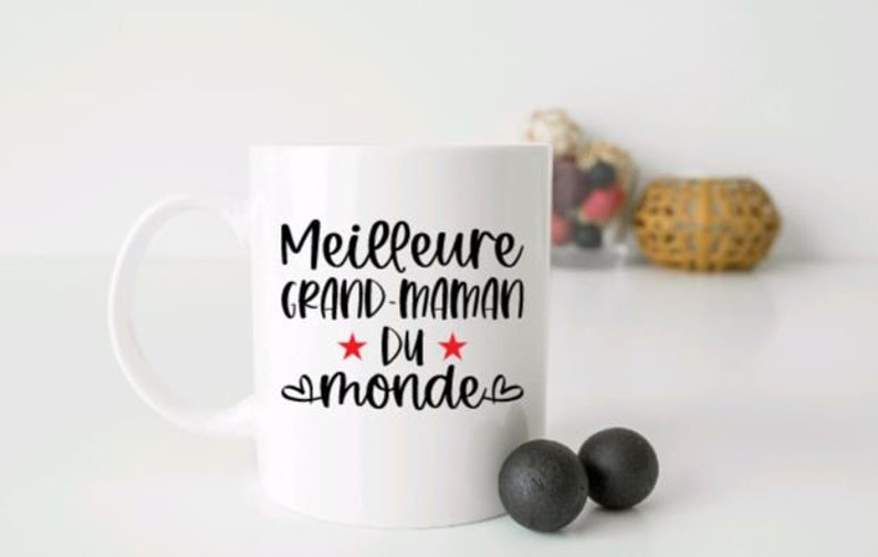 May include: White ceramic mug with a black inscription that reads "Meilleure Grand-Maman du monde" with two red stars and hearts.