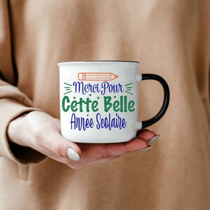 May include: White ceramic mug with a black handle. The mug has a black rim and a design of a pencil, stars, and the text "Merci Pour Cette Belle Ann&eacute;e Scolaire".