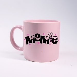 May include: Pink ceramic mug with a black graphic that says "Mamie" with pink hearts and stars around the text.