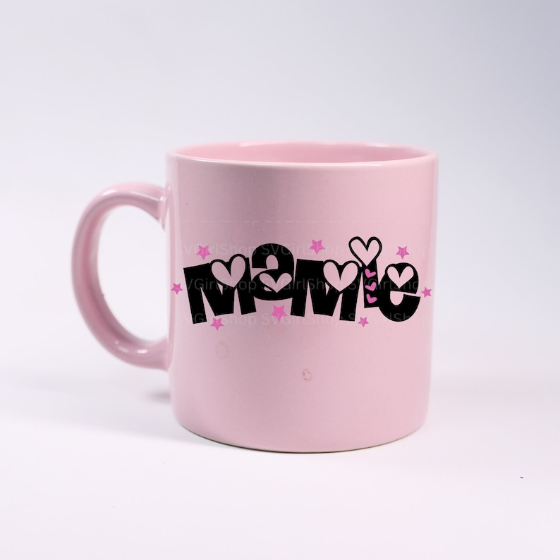 May include: Pink ceramic mug with a black graphic that says "Mamie" with pink hearts and stars around the text.
