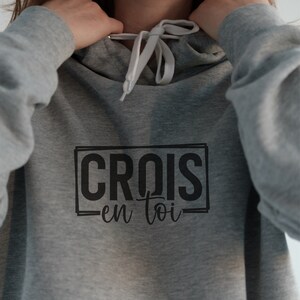 May include: Grey hooded sweatshirt with a black graphic that says "CROIS en toi" in a rectangular box.