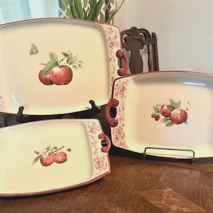 May include: Set of three rectangular serving platters with red floral and apple designs. Each platter has a cream-colored background, red handles, and a red floral border. The largest platter measures approximately 16 inches long.