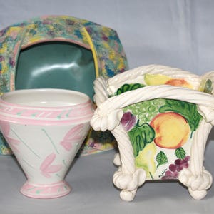 May include: Three ceramic planters, one with a pink and white floral design, one with a white rope design and a fruit print, and one with a blue and yellow abstract design.