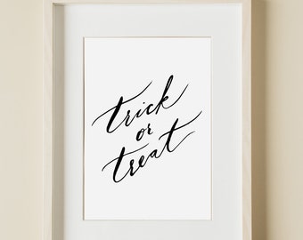 Puede incluir: Un marco de madera de color claro que contiene una impresión blanca con el texto negro escrito a mano Trick or Treat. Debajo del marco, el texto PRINT CODES DESIGN es visible en una fuente sans-serif simple y oscura sobre el fondo liso.