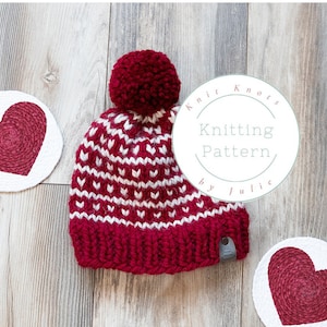 May include: A red and white knitted hat with a pom pom on top. The hat has a heart pattern and the text "Knit Knots Knitting Pattern by Julie" is on a white circle.