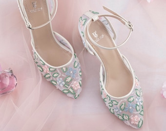 May include: A pair of white bridal shoes with delicate floral embroidery in shades of pink, blue, and green. The shoes have a delicate ankle strap with a buckle closure. The brand name "BRIDAL BOX" is visible on the insole.