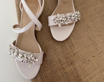 May include: A pair of white satin sandals with ankle straps and a crystal embellishment on the toe.