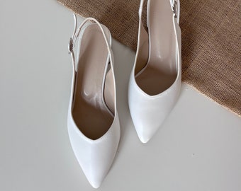May include: A pair of white leather slingback pumps with pointed toes. The shoes have a buckle closure on the ankle strap.