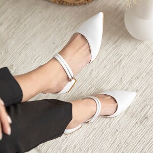 May include: White leather heeled shoes with a pointed toe and double straps around the ankle.