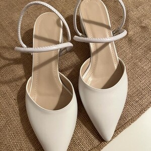 May include: A pair of white pointed-toe heeled sandals with ankle straps. The straps are made of a braided material.