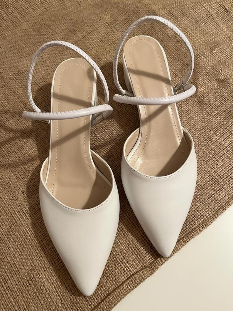 May include: A pair of white pointed-toe heeled sandals with ankle straps. The straps are made of a braided material.