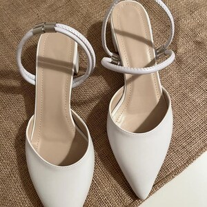 May include: A pair of white pointed-toe heeled shoes with ankle straps. The straps have a silver buckle detail.