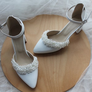 May include: White satin bridal shoes with ankle straps and pearl embellishments.