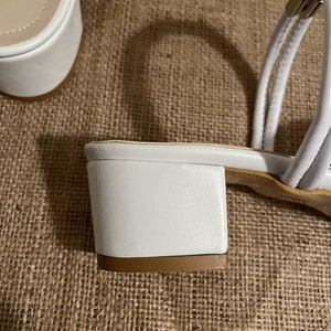 May include: White leather heeled sandals with a block heel and ankle strap.