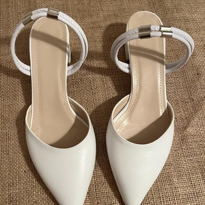 May include: White pointed-toe heeled sandals with a double strap ankle closure and silver accents.
