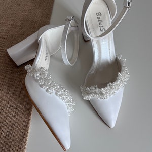 May include: White satin bridal heels with a chunky block heel and a pearl trim around the ankle strap. The heels have the brand name "BulutS" written on the inside of the strap.