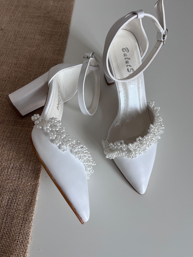 May include: White satin bridal heels with a chunky block heel and a pearl trim around the ankle strap. The heels have the brand name "BulutS" written on the inside of the strap.