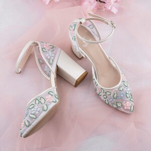 May include: White high-heeled shoes with a floral design. The shoes have a chunky heel and an ankle strap.