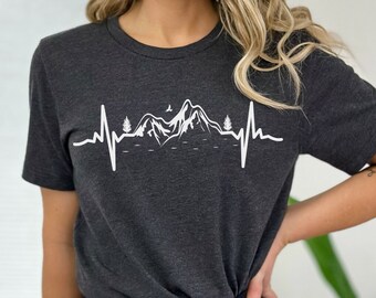 Könnte beinhalten: Ein dunkelgraues T-Shirt mit einem weißen Aufdruck einer Bergkette mit einer Herzschlaglinie und einem Vogel, der über den Bergen fliegt.