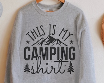 May include: A gray sweatshirt with the text "This is my camping shirt" in black lettering. The text is surrounded by a graphic of mountains and stars.