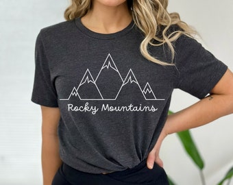 Op de afbeelding: Een donkergrijs T-shirt met een witte omtrek van bergen en de tekst "Rocky Mountains".