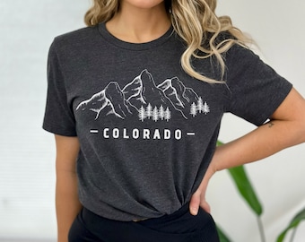 Op de afbeelding: Een donkergrijs T-shirt met een witte afbeelding van bergen en bomen. De tekst "_COLORADO_" is onder de afbeelding gedrukt.