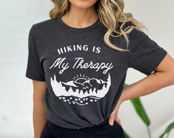 May include: A dark gray t-shirt with a white graphic that says "Hiking is My Therapy" with a mountain range and a sun graphic.