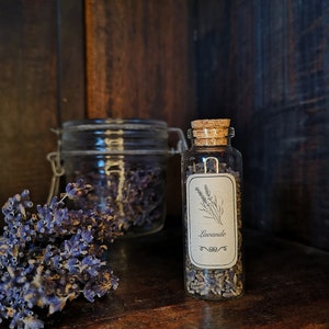 May include: A small glass jar with a cork lid filled with dried lavender flowers. The jar has a label that says "Lavande" in cursive writing.